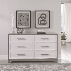 a white dresser with two pictures on the wall above it and a rug in front of it