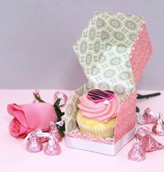 a cupcake in a box with pink frosting on top next to some candy