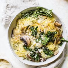 a white bowl filled with pasta, mushrooms and spinach sprinkled with parmesan cheese