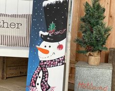 there is a snowman painted on the side of a door with a christmas tree next to it