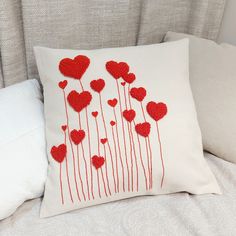 a pillow with red hearts on it sitting on top of a bed next to pillows