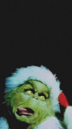 the grinch is wearing a santa hat and holding a cell phone to his ear