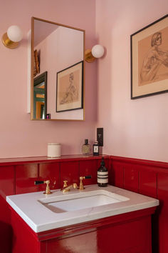 a bathroom with pink walls and gold fixtures, including a white sink in front of a mirror