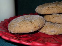 three cookies sitting on top of a red plate next to a glass of white milk