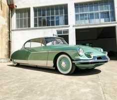 an old green car is parked in front of a large building with two garage doors