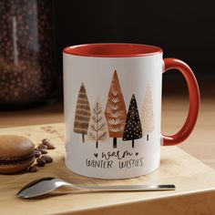 a red and white coffee mug sitting on top of a wooden table next to a spoon