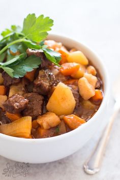 a white bowl filled with meat and vegetables on top of a table next to a spoon