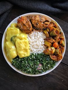 a white plate topped with rice, meat and veggies on top of a wooden table