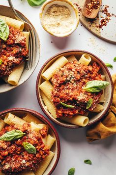 three bowls filled with pasta and sauce on top of a white table next to bread