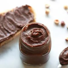 peanut butter in a jar next to toasted pieces of bread on a white surface