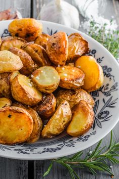 a white plate topped with cooked potatoes on top of a wooden table next to garlic