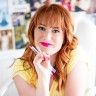 a woman with long red hair is posing for a photo while holding her hand on her chin