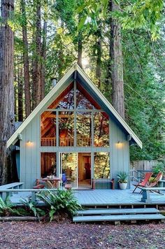 a small cabin in the woods with lots of trees and chairs on the front porch