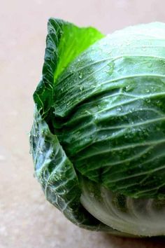 a head of lettuce with water droplets on it's leaves sitting on the ground