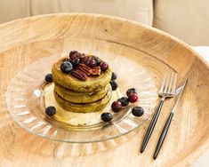 a stack of pancakes with blueberries, pecans and maple syrup on a glass plate