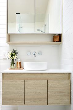 a bathroom with a white sink and wooden cabinet under a large mirror on the wall