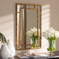 a mirror and vase with white flowers on a table in front of a wall mounted mirror