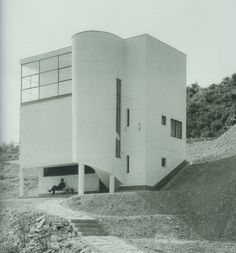 a black and white photo of a person sitting on a bench in front of a building