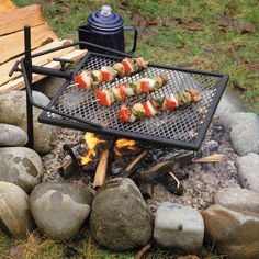 an outdoor grill with food cooking on it and fire in the ground next to rocks