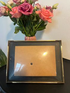 a vase filled with pink and purple flowers on top of a table next to a framed photograph