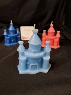 three plastic castle shaped candles sitting on top of a black cloth covered table with a name tag