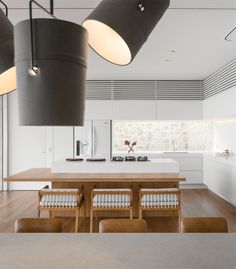 an open kitchen and dining room with modern lighting fixtures in the center, along with wooden tables and chairs