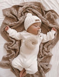 a baby is sleeping on a blanket and wearing a white knitted outfit with a pom - pom