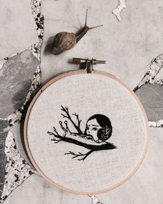 a hand embroidered picture of a woman's face on a tree branch next to a snail