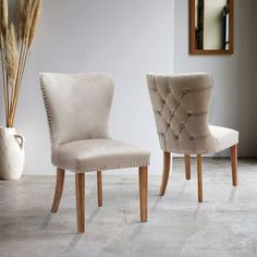 two beige chairs sitting next to each other in front of a white vase and mirror