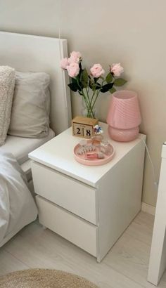 a white nightstand with pink flowers on it next to a night stand and bedding