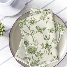 three napkins with green flowers on them sitting on a plate next to a cup and saucer