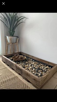 a wooden box filled with rocks on top of a floor next to a potted plant