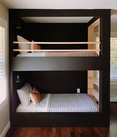 two bunk beds in a room with wood floors and black walls, one has a white pillow on it