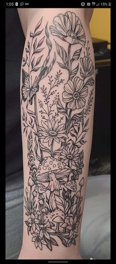 a woman's leg with flowers and leaves on it, in black ink by tattoo artist