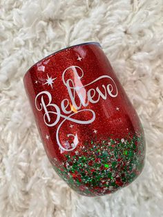 a red wine glass with the words believe painted on it sitting on a white carpet