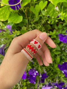 a woman's hand holding two bracelets in front of purple flowers