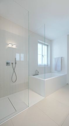 a large white bathroom with a glass shower door and tub in the corner, next to a window