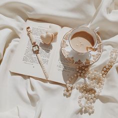 a cup of coffee on top of an open book next to pearls and a necklace