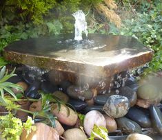 a fountain in the middle of some rocks and plants with water coming out of it