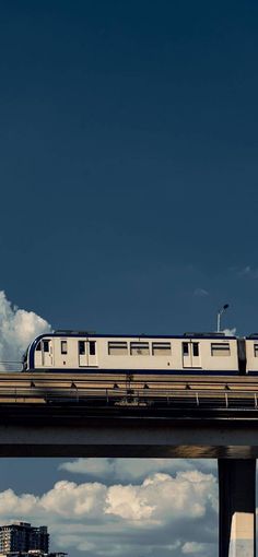 a passenger train traveling over a bridge in the middle of the day with blue sky and clouds behind it