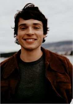 a young man smiling at the camera with mountains in the backgrouund behind him