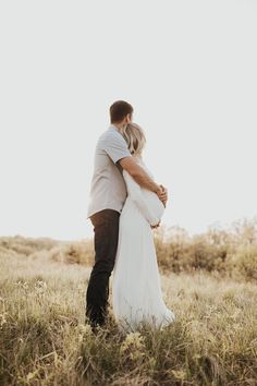 a bride and groom embracing in the middle of a field with tall grass on either side