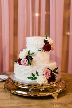 a wedding cake with flowers on it sitting on top of a table next to a pink curtain