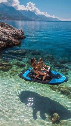 two women on a blue and black jet ski in clear water next to rocky shore