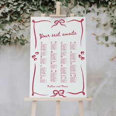 a wedding seating chart on an easel in front of a wall covered with greenery