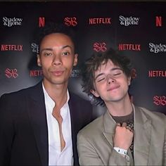 two men standing next to each other in front of a red wall with netflix logo on it