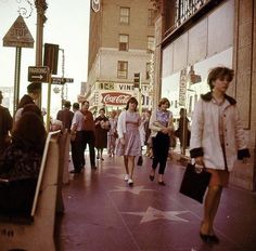 people walking down the sidewalk in front of shops and stores on a busy city street