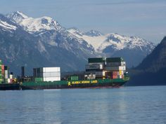 a large green and white cargo ship in the water with mountains in the back ground