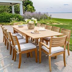 an outdoor dining table and chairs with flowers on the table in front of some water