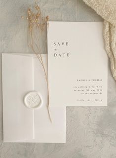 a white save the date card with a ring on it next to an envelope and some dried flowers